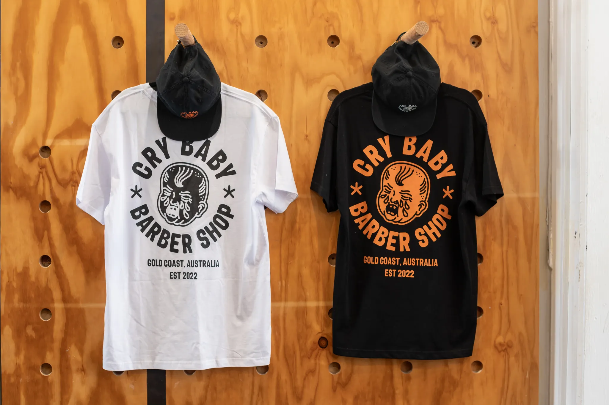 Cry Baby Barber Shop t-shirts and caps hanging on the merch wall